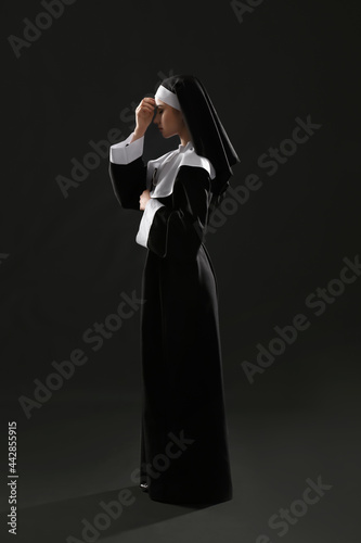 Young praying nun on dark b...