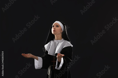 Young praying nun on dark b...