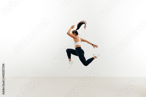 Side view of woman with muscular body jumping against white wall