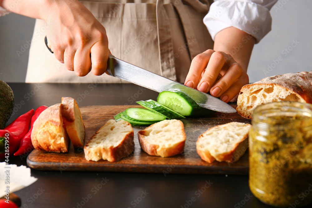 Woman cutting cucumber for tasty sandwiches on table