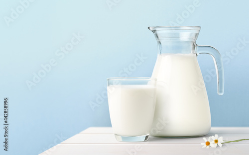 Glass and Jug of fresh milk on white wooden table.