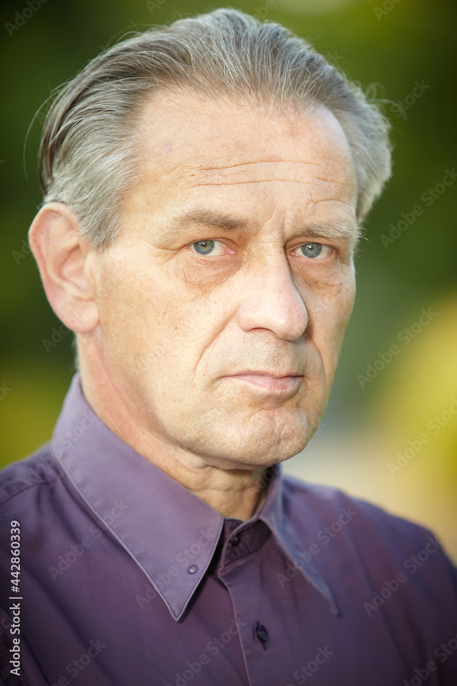 Obraz premium Older man in violet shirt posing in park for portrait