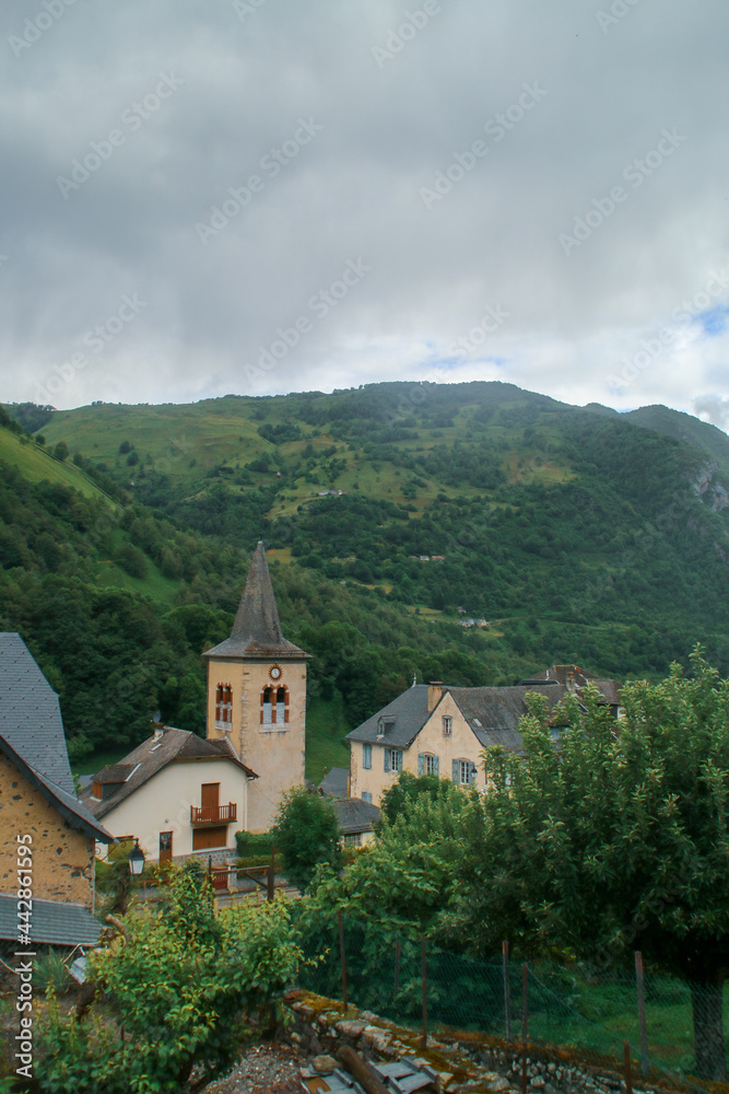 Fotografía de Urdos, pequeño pueblo de montaña rodeado de bosque y nubes en un día lluvioso. Église Sainte-Marie-Madeleine (Iglesia de Santa María Magdalena) en Urdos, Pirineos franceses.