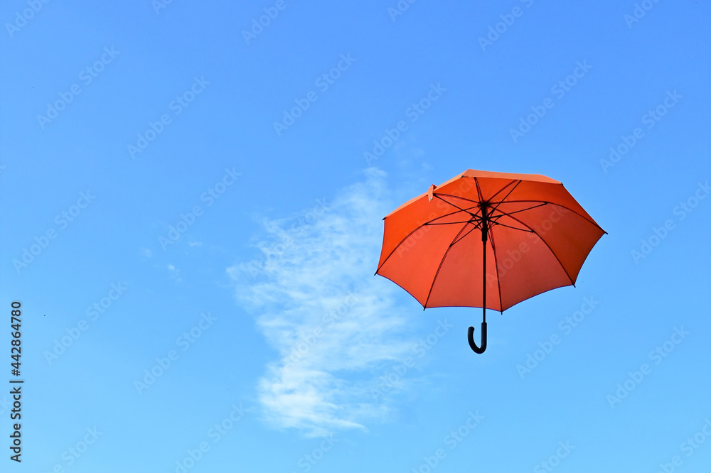 An orange umbrella flying away into the blue sky. Weather changes. Background. Copy space