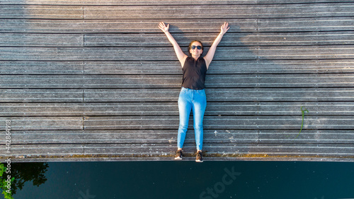 Vacation, enjoyment and freedom concept. Top aerial view from drone lifestyle portrait of young woman on a wooden riverside next to the water of the river. High quality photo