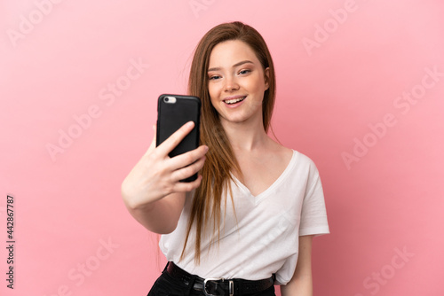 Teenager girl over isolated pink background making a selfie with mobile phone