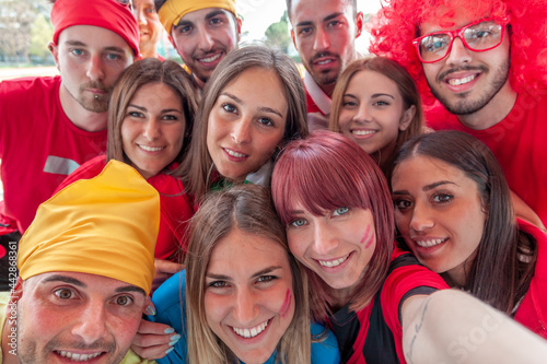 group of fans dressed in red color takes a selfie in the stands of a stadium