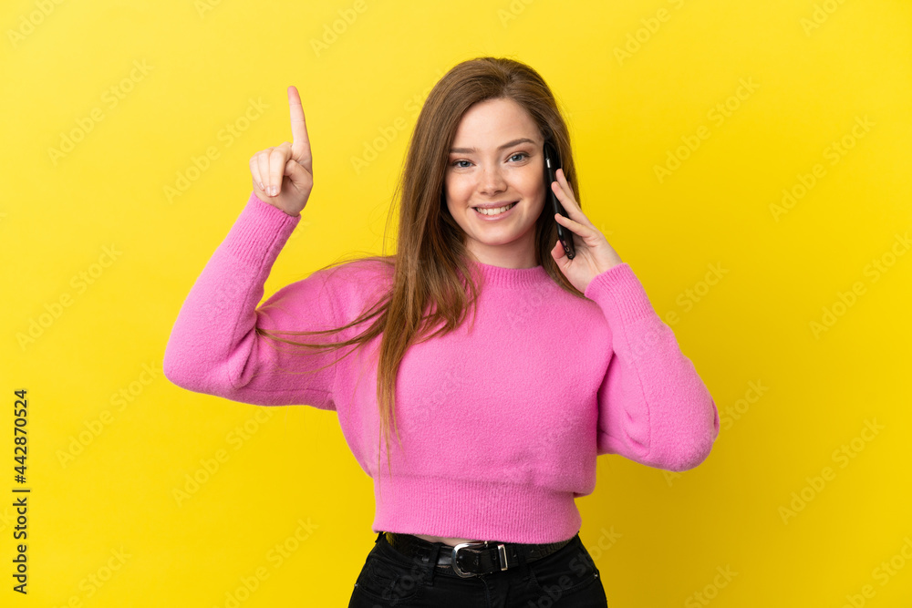 Teenager girl using mobile phone over isolated yellow background pointing up a great idea Teenager girl using mobile phone over isolated yellow background pointing up a great idea