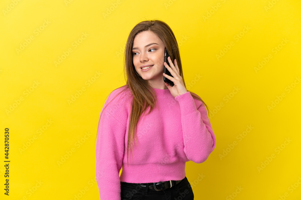 Teenager girl using mobile phone over isolated yellow background looking to the side and smiling Teenager girl using mobile phone over isolated yellow background looking to the side and smiling