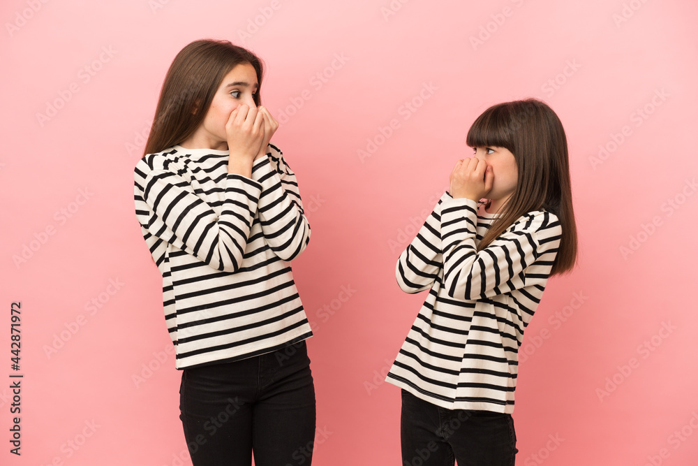 Little sisters girls isolated on pink background is a little bit nervous and scared putting hands to mouth Little sisters girls isolated on pink background is a little bit nervous and scared putting hands to mouth
