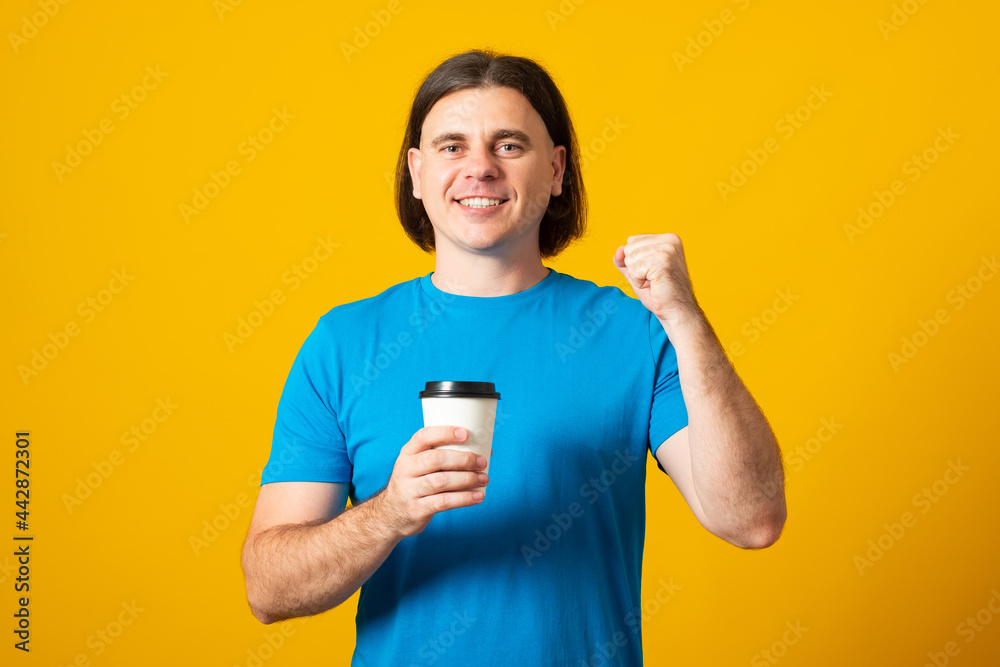 Positive male has trendy hairdo holds paper cup of coffee, going to have break and drink hot beverage, isolated on yellow background. People and lifestyle concept.