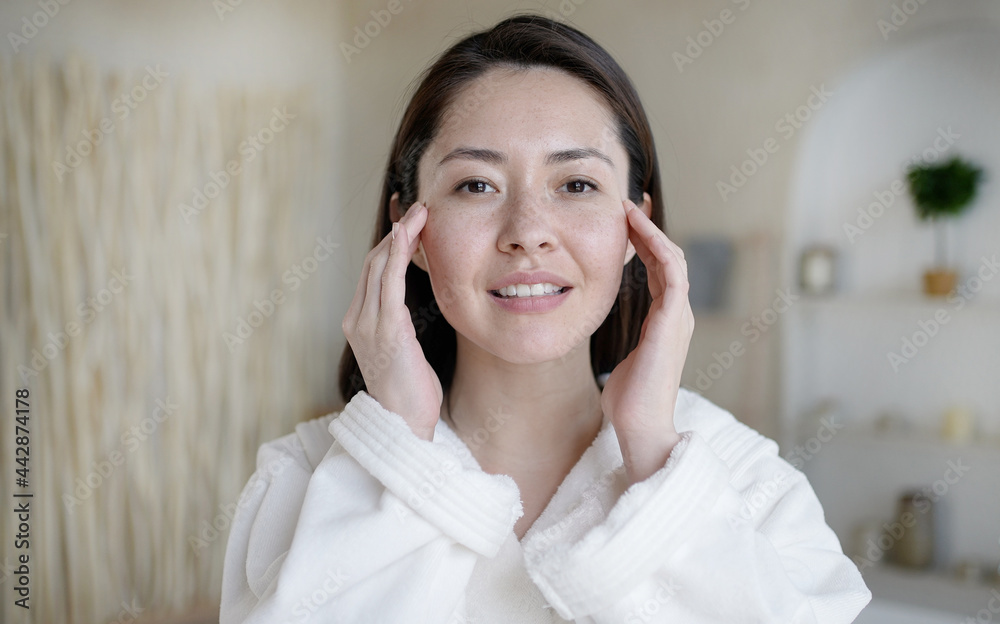 Attractive multi ethnic lady looking in mirror touching healthy soft face skin in bathroom. Young mixed race asian woman doing massage satisfied with facial procedures skincare concept. Attractive multi ethnic lady looking in mirror touching healthy soft face skin in bathroom. Young mixed race asian woman doing massage satisfied with facial procedures skincare concept.