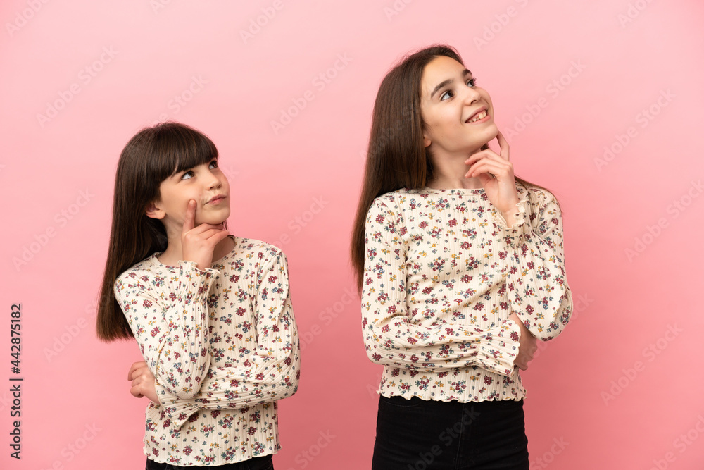 Little sisters girls isolated on pink background thinking an idea while looking up