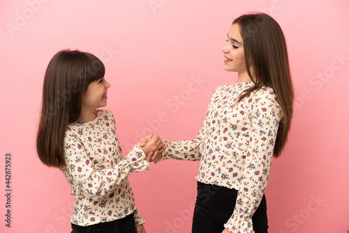 Little sisters girls isolated on pink background handshaking after good deal