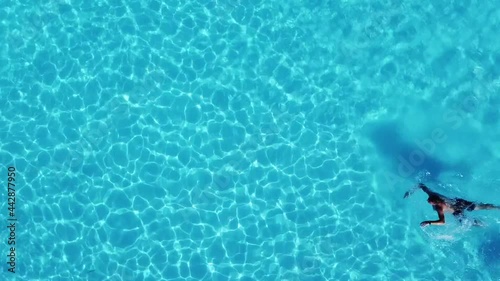 Man swims at swimming pool. Rippling water in swimming pool top down aerial view. Water surface refracting sunlight