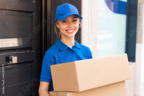 Young delivery woman at outdoors holding boxes with happy expression