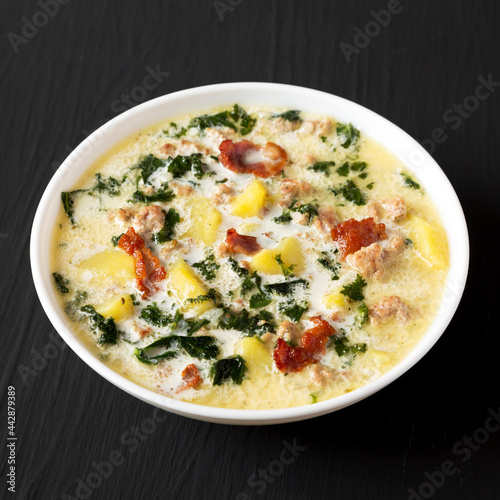 Homemade Zuppa Toscana with Kale and Bread in a white bowl on a black background, side view.