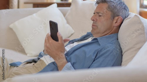 Medium Shot of Middle Aged Man Slouched On Sofa Using Smartphone  photo