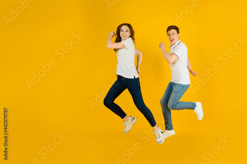 Portrait of a young happy couple man and woman in white t-shirts jumping and laughing on a yellow background.
