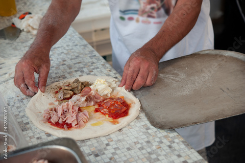 Pizzaiolo puts a four season pizza on the peel, ready to bake. Italian pizzeria.