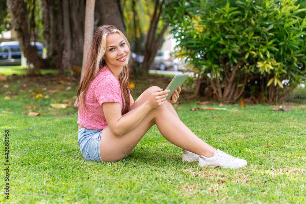 Fototapeta premium Young pretty woman at outdoors holding a tablet with happy expression