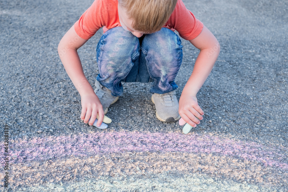 Fototapeta premium Boy with both hands draws a rainbow on the sidewalk on the pavement