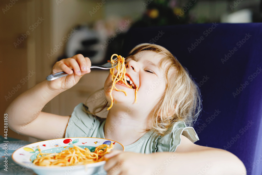 Adorable toddler girl eat pasta spaghetti with tomato bolognese with minced meat. Happy preschool child eating fresh cooked healthy meal with noodles and vegetables at home, indoors.