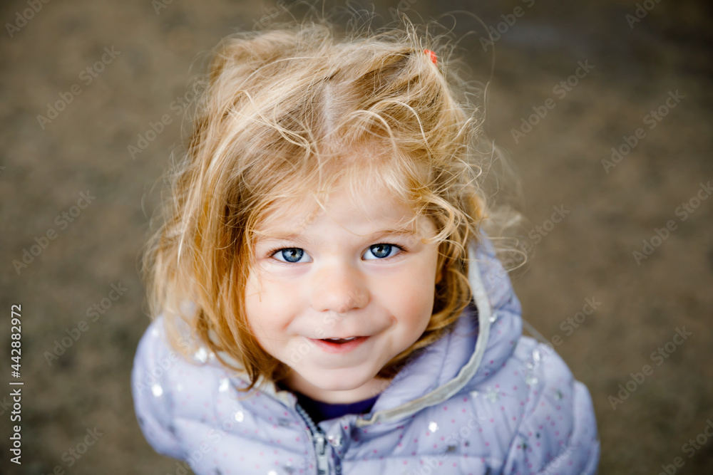 Portrait of happy smiling toddler girl outdoors. Little child with blond hairs looking and smiling at the camera. Happy healthy child enjoy outdoor activity and playing. Portrait of happy smiling toddler girl outdoors. Little child with blond hairs looking and smiling at the camera. Happy healthy child enjoy outdoor activity and playing.