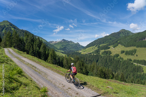 happy senior woman riding her electric mountain bike up to thr famous mountain village of Damuels in the Bregenz Forest mountain of Vorarlberg, Austria © Uwe