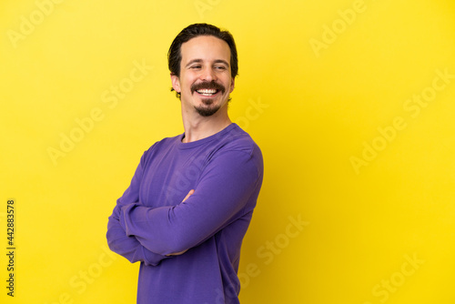Young caucasian man isolated on yellow background with arms crossed and happy