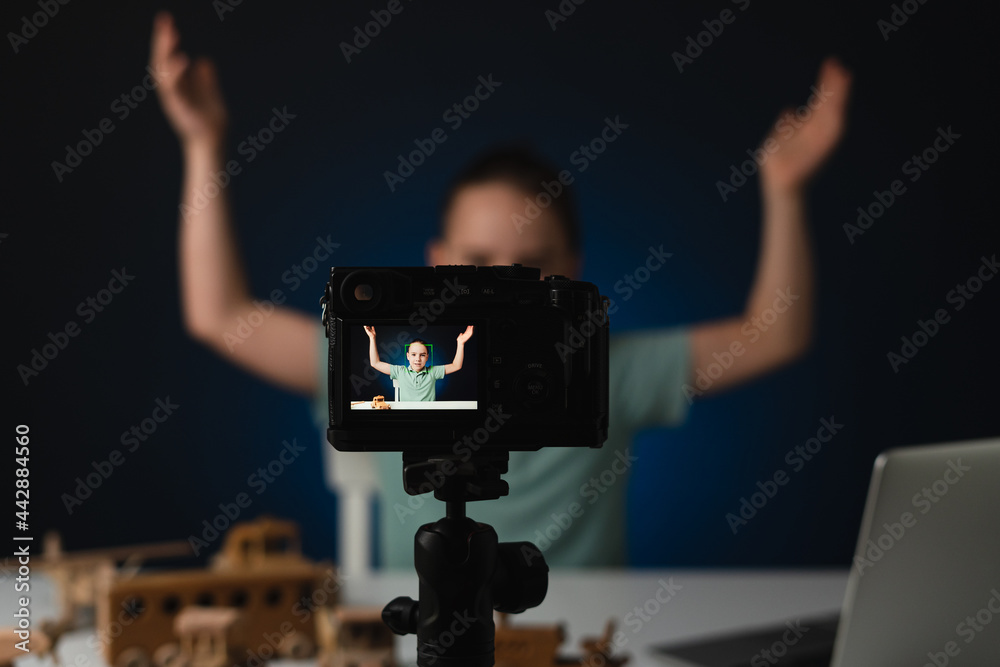 Kid blogger filming video on camera using the laptop, indoors. Online reviewing. Promoting eco wooden toys. Kid recording his gameplay for vlog.