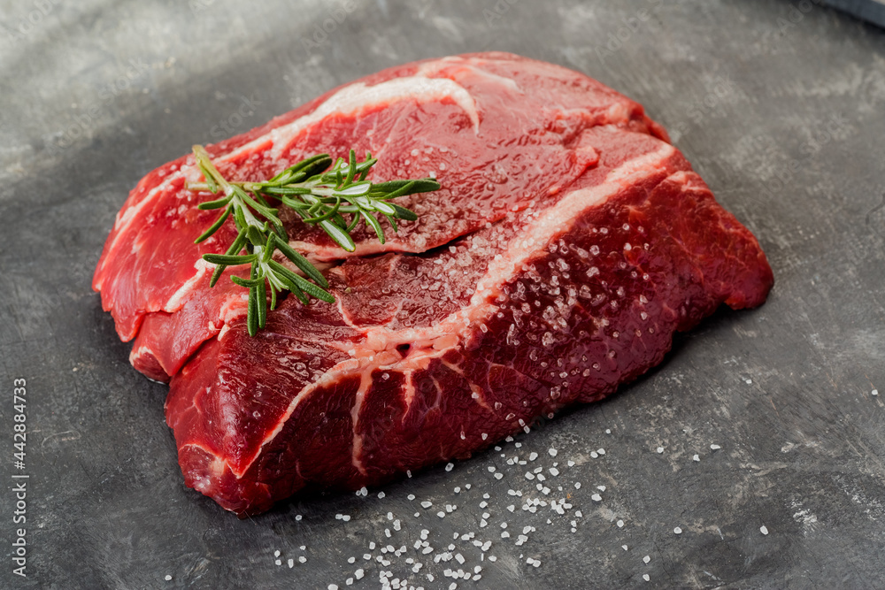 Raw beef steak with rosemary on a dark background