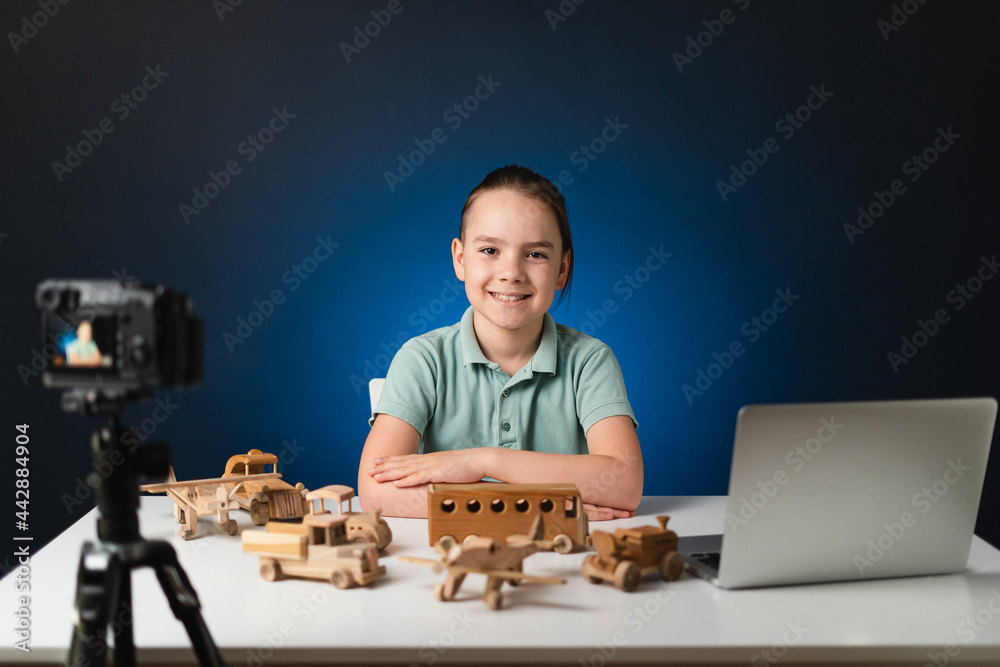 Kid blogger filming video on camera using the laptop, indoors. Online reviewing. Promoting eco wooden toys. Kid recording his gameplay for vlog. Kid blogger filming video on camera using the laptop, indoors. Online reviewing. Promoting eco wooden toys. Kid recording his gameplay for vlog.