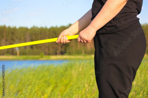 Fisherwoman with a yellow fishing rod on a background of a pond and a blue sky on a summer sunny day. Woman catching fish. Active leisure and recreation in nature reserve. Angling on a bank of a river
