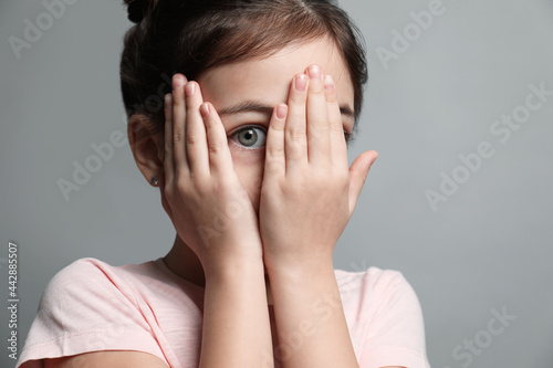 Little girl feeling fear on grey background, closeup photo