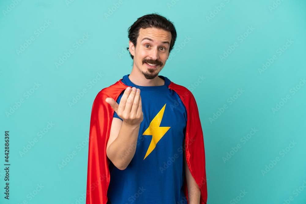 Super Hero caucasian man isolated on blue background inviting to come with hand. Happy that you came