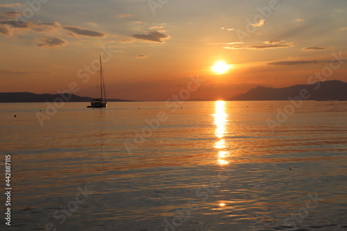 Yacht on the sea on a summer evening against the backdrop of the setting sun, a mountain range on the horizon, Croatia © Vasilisa