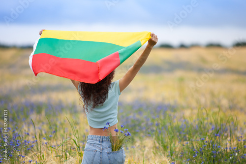 Foto Young woman holding flag of Lithuania in a rye field with blue cornflowers