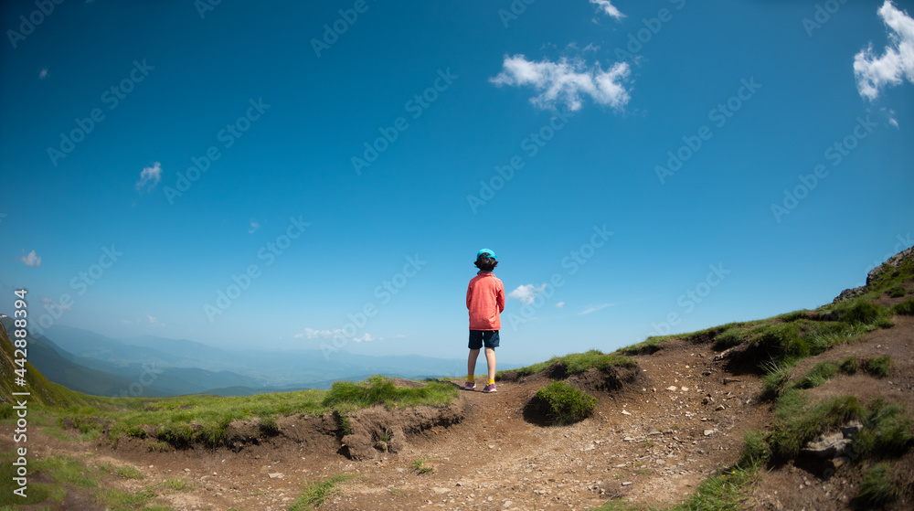 A child stands on the top of a mountain and looks into the distance