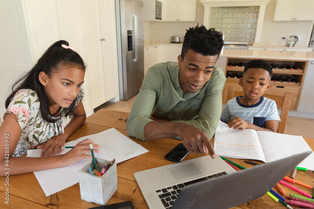 Happy african american father using laptop, daughter and son doing homework at home Happy african american father using laptop, daughter and son doing homework at home