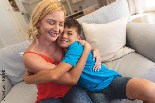 Caucasian mother and son sitting on couch embracing and smiling at home