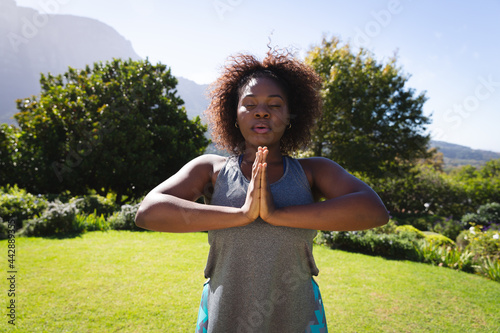 Midsection of african american woman practicing yoga with eyes closed in sunny garden