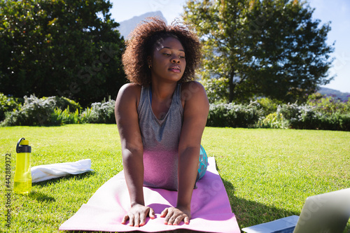 African american woman exercising on yoga mat in sunny garden