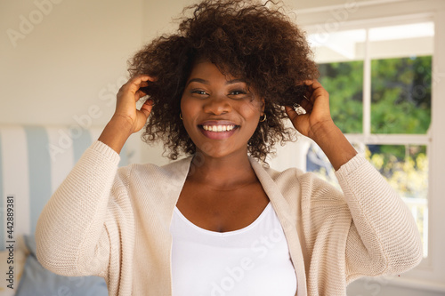 Portrait of smiling african american woman touching her hair sitting on bed at home
