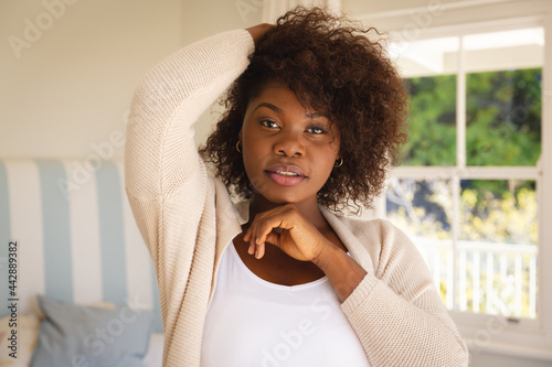 Portrait of african american woman touching her hair sitting on bed at home