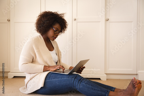 Happy african american woman working in bedroom, sitting floor and using laptop
