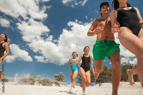 a group of friends consisting of men and women running on the beach in the sea