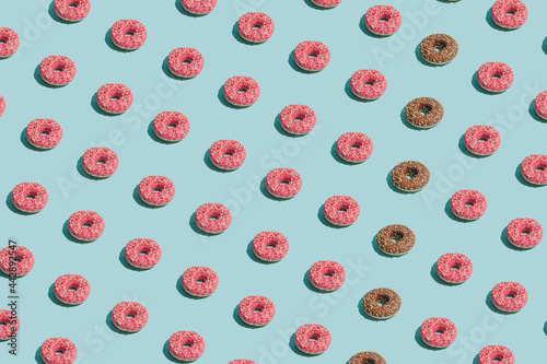 Creative summer vibes concept with tasty pink and brown doughnuts on bright blue background. Sweet, delicious food idea, minimalistic irregular pattern composition.