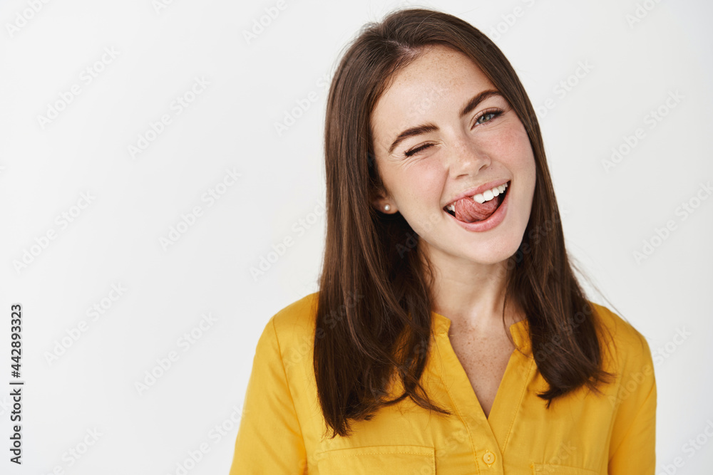 Close-up of pretty and funny young woman showing tongue, smiling and winking at camera with joy, standing over white background Close-up of pretty and funny young woman showing tongue, smiling and winking at camera with joy, standing over white background