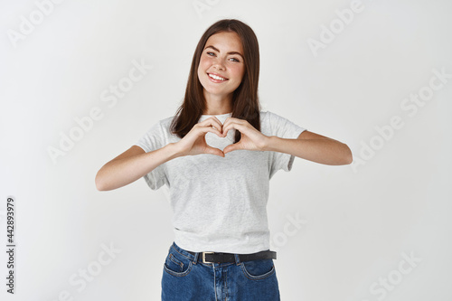 Cute young woman showing heart sign, I love you gesture, wishing happy valentines day, standing over white background photo